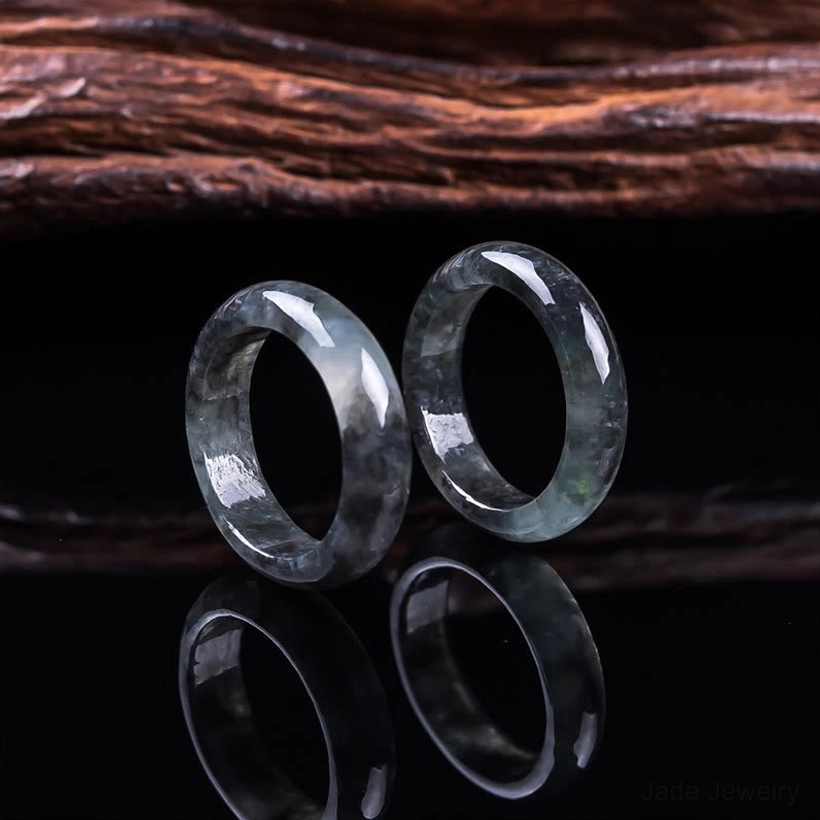 Two matching natural jade prosperity rings in polished dark jade displayed with mirrored reflections on black background