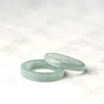 Stacked genuine jade prosperity rings in light green, displayed at an oblique angle on traditional Chinese calligraphy background