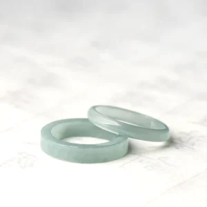 Stacked genuine jade prosperity rings in light green, displayed at an oblique angle on traditional Chinese calligraphy background
