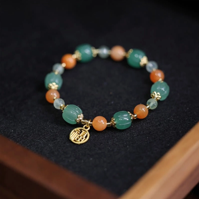 Golden Silk Jade pumpkin bead bracelet flat lay top view, circular design with green and orange gemstones and gold Fu pendant