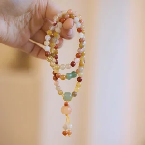 Close-up side view of golden jade beads with metal spacer and tassel pendant held in hand showing bead detail