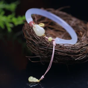 Hetian jade rabbit bangle bracelet displayed on natural twig nest with green foliage showing full decorative design