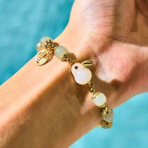 Jade rabbit abundance bracelet worn on wrist showing white jade rabbit charm, gold Fu character pendant, and elastic string detail on light background