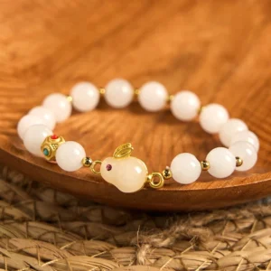 Jade Rabbit Bracelet flat lay overhead - White jade beads with purple-eyed rabbit charm and gold accents on woven mat background