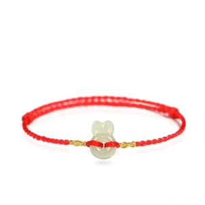 Pale jade rabbit charm on red braided cord with decorative gold knots, close-up view