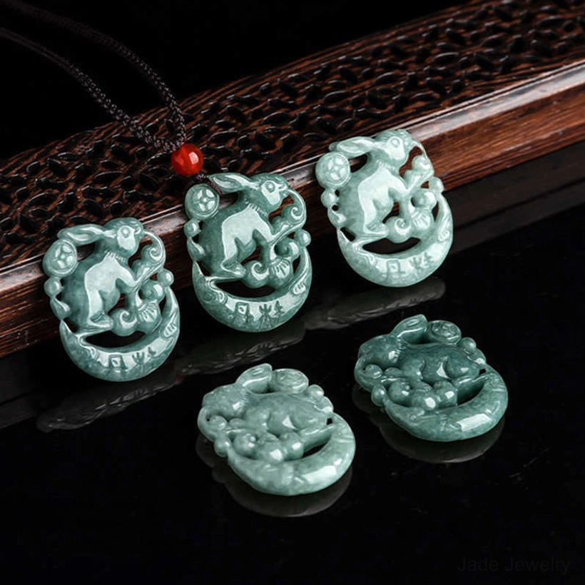 Collection of five matching green jade rabbit crescent moon pendants displayed on wooden and glossy black surface, showing consistent craftsmanship