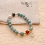 Jade red agate pearl bow tie bracelet flat lay with teal beads and white flower pendant on embroidered pouch