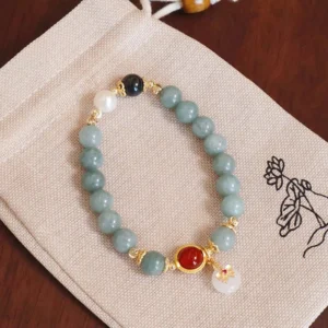 Handmade jade beaded prosperity bracelet with red agate center and gold-toned hardware on lotus pouch
