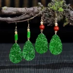 Handcrafted jade drop earrings with red agate beads and sterling silver posts in water droplet design, displayed on natural twigs with moss background