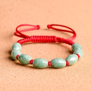 Top-down flat lay of jade beaded red string bracelet showing green jade stones and red spacers on terracotta surface