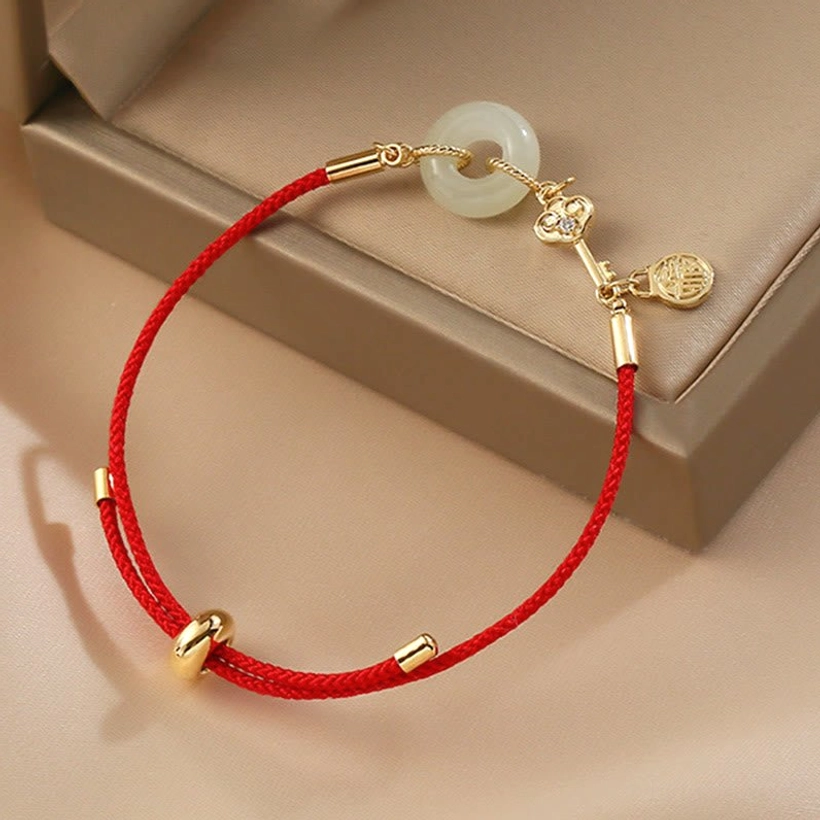 Three-quarter view of red string jade bracelet with stone-inlaid heart charm next to brown jewelry box