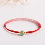 Handmade jade lucky bead bracelet with red braided cord and gold spacers, side angle view