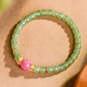 Jade rhodonite bracelet with gold spacers, flat lay on neutral fabric background showing bead arrangement and color composition