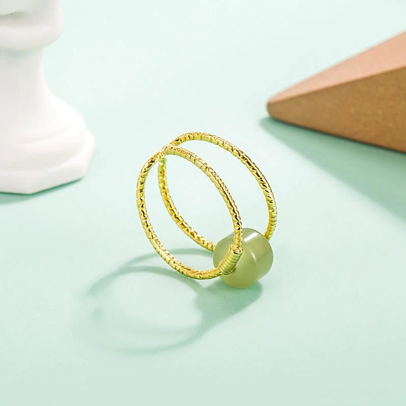 Natural jade stone adjustable cuff ring with gold-tone twisted bands, side angle view with light green backdrop