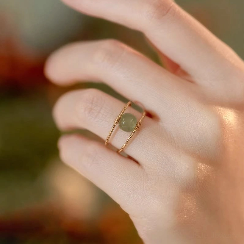 Close-up of adjustable jade ring being worn on hand, showing twisted gold band and small round jade bead accent in daily wear