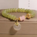 Handmade jade rose quartz peace buckle bracelet with green beads, pink quartz accents, and gold spacer bead on brown jewelry tray