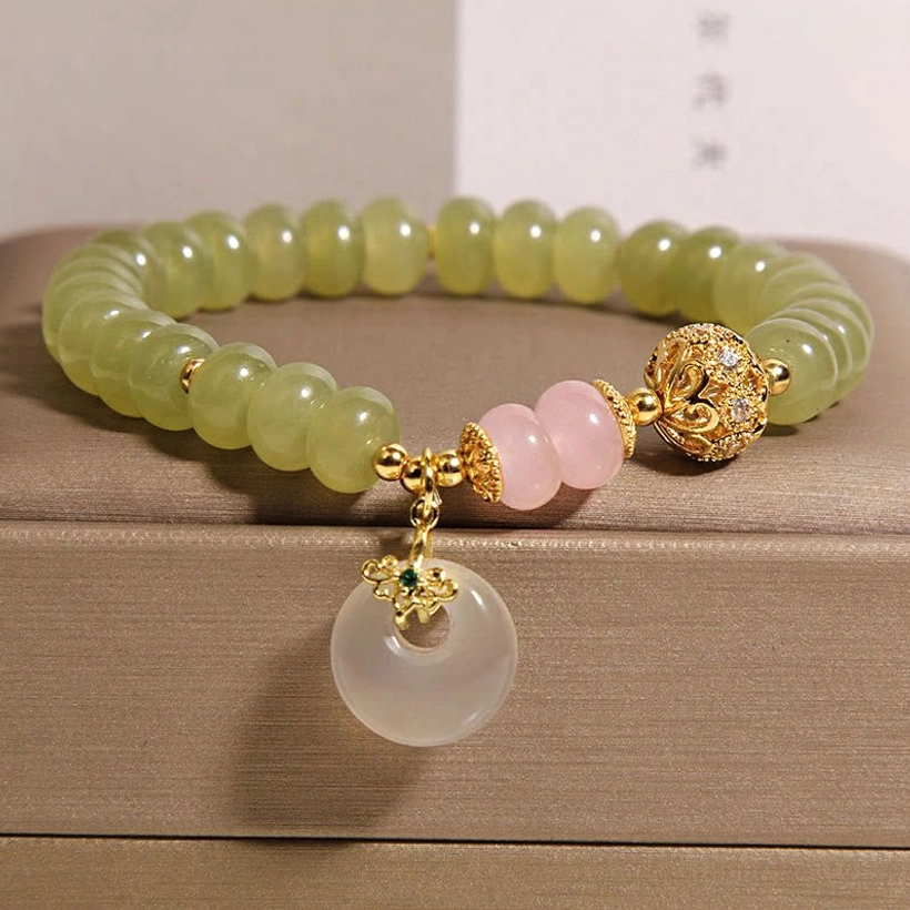 Handmade jade rose quartz peace buckle bracelet with green beads, pink quartz accents, and gold spacer bead on brown jewelry tray