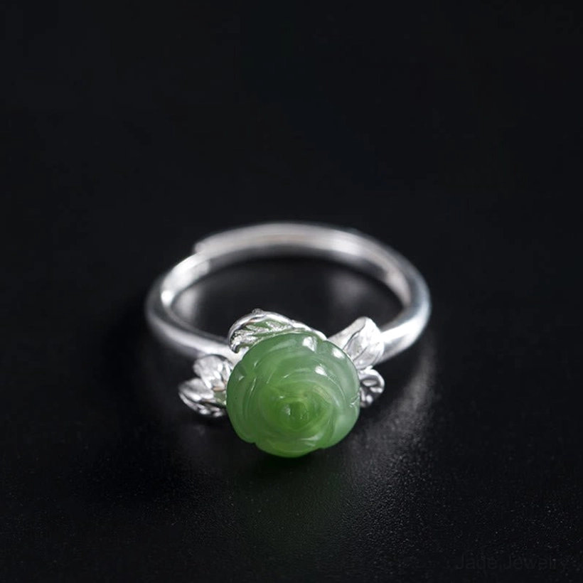 Jade rose silver ring displayed on dark wooden surface emphasizing the carved rose carving and leaf metalwork