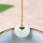 Natural jade round pendant necklace with golden chain resting on ceramic bowl, front close-up view