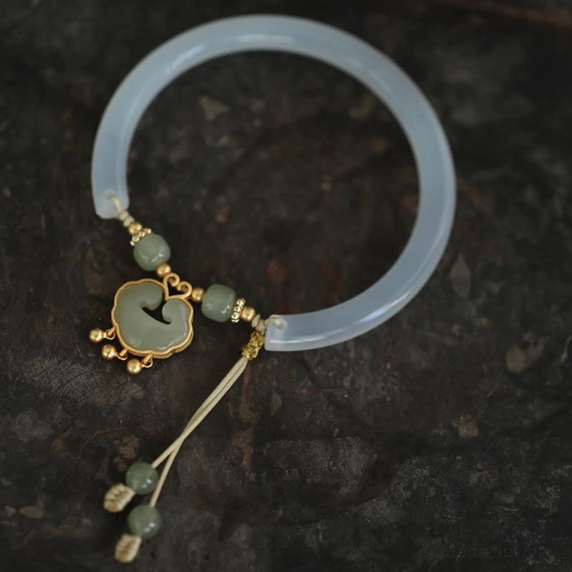 Top-down flat lay of chalcedony jade bangle on dark textured background, showing smooth semi-transparent band and detailed ruyi pendant