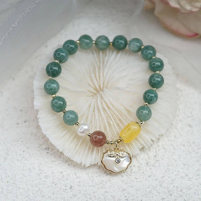 Green jade Ruyi lock bracelet with sea shell charm displayed on white seashell and sand background - top view flat lay