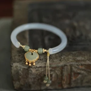 Top-down view of chalcedony jade bangle bracelet displayed on vintage stone, featuring translucent band and gold-mounted jade ruyi pendant