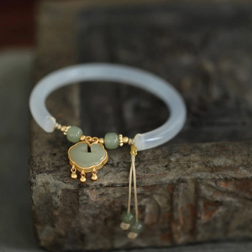Top-down view of chalcedony jade bangle bracelet displayed on vintage stone, featuring translucent band and gold-mounted jade ruyi pendant