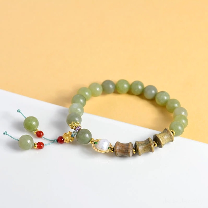 Jade sandalwood beaded bracelet overhead shot with round jade beads pearl charm and tassel on warm background
