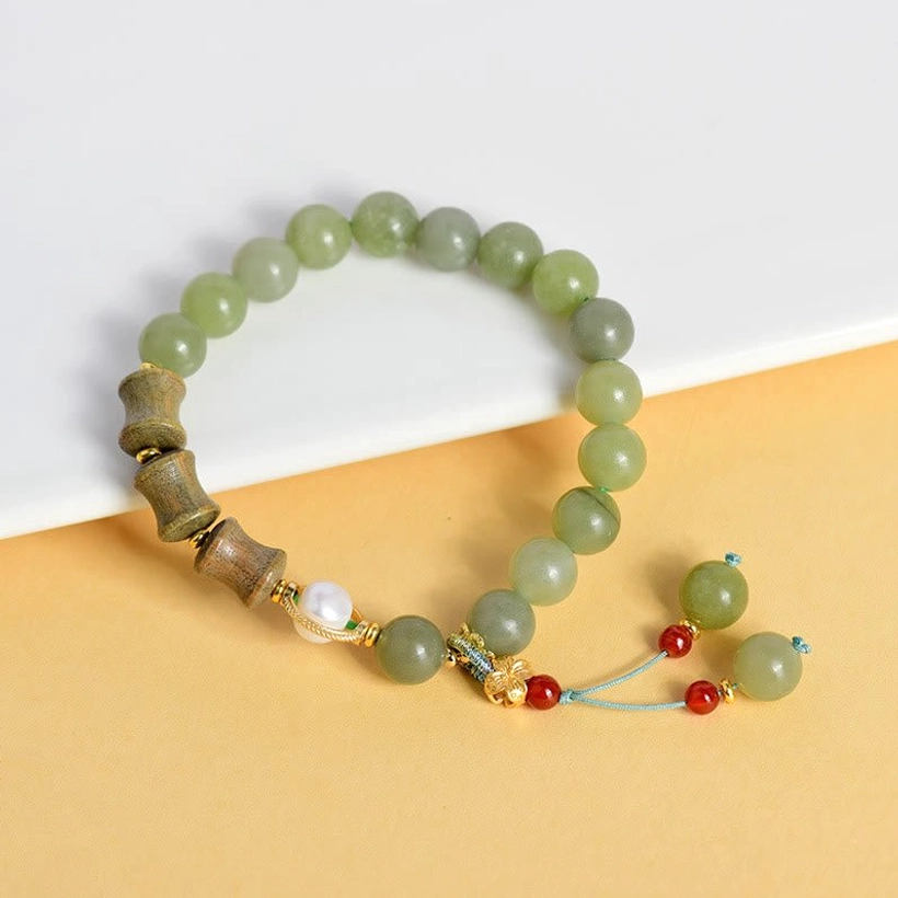 Jade sandalwood pearl bracelet with red and green bead tassel charm on light background