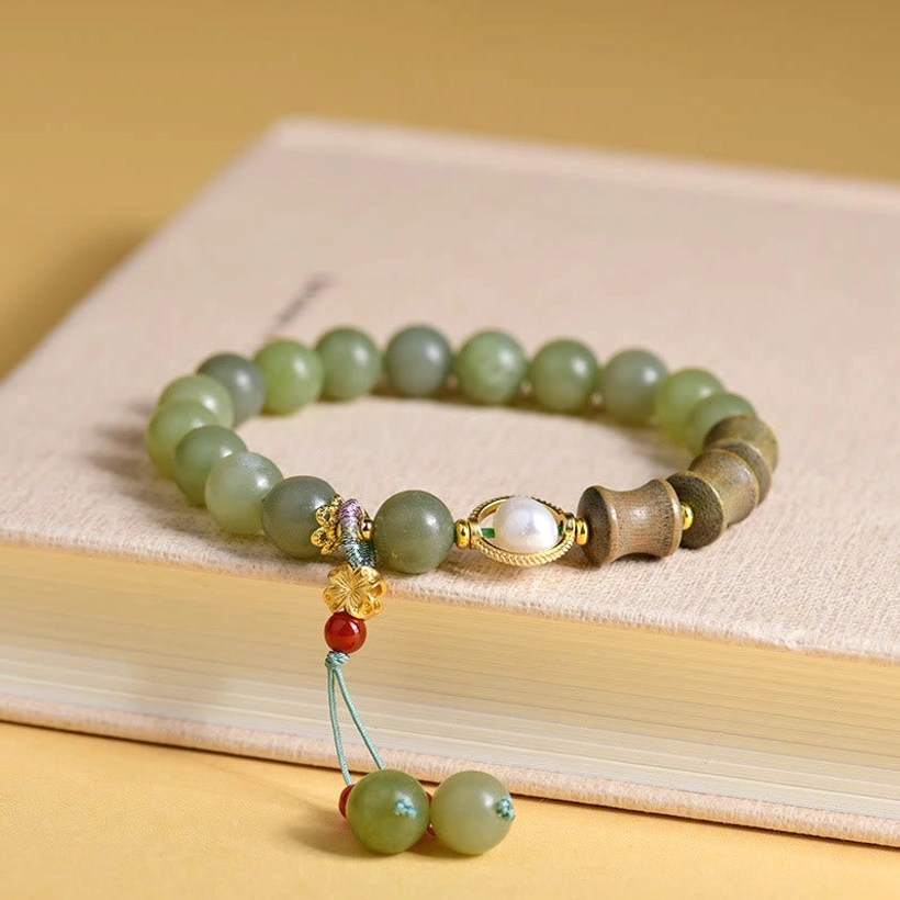 Green jade sandalwood bamboo pearl prosperity bracelet flat lay on beige book with tassel charm