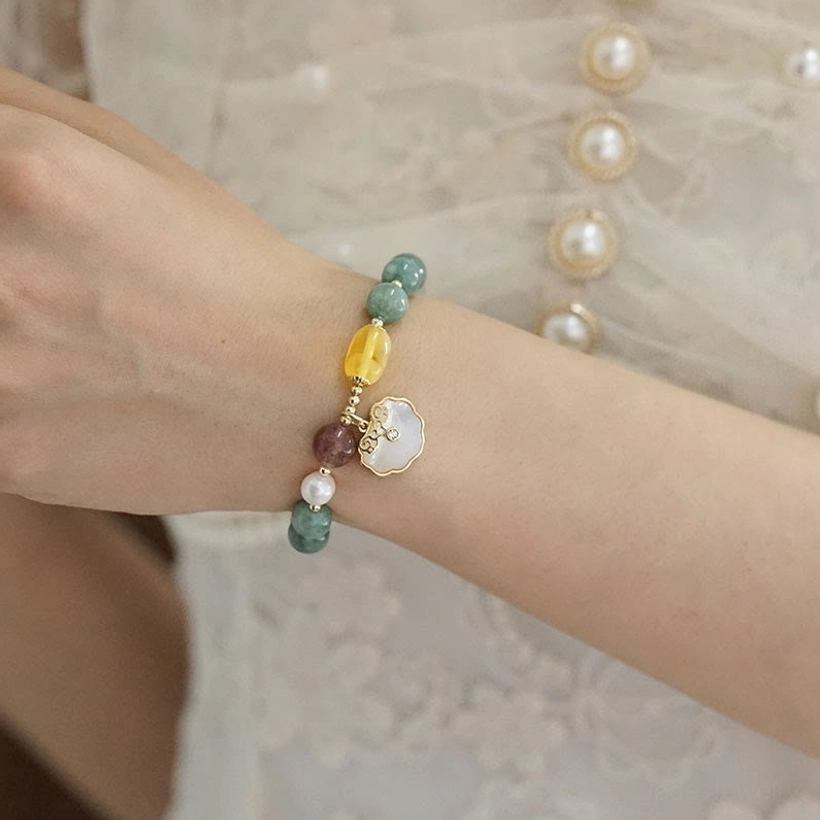Jade luck bracelet on wrist with sea shell pendant hanging beside - side oblique view with pearl lace fabric