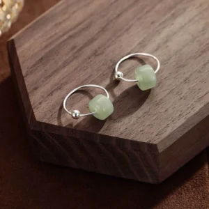 Side angle view of jade hoop earrings displaying cylindrical jade stone secured on thin silver hoop