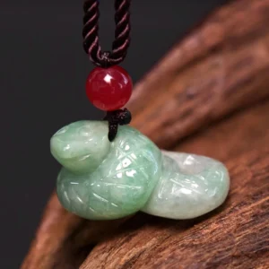 Natural jade snake zodiac pendant necklace close-up detail view displaying carved scales, coiled design, red accent bead, and hand-waxed brown cord on wooden surface