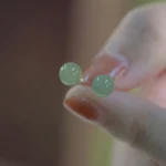 Natural round jade stud earrings 8mm displayed on fingertip with sterling silver posts, close-up view