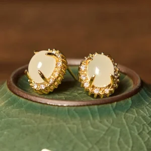 Authentic Hetian jade stone earrings on green ceramic surface, oblique angle showing metal setting detail