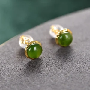 Pair of natural jade stud earrings with clear acrylic earring backs on grey suede surface, demonstrating included ear backs for comfort
