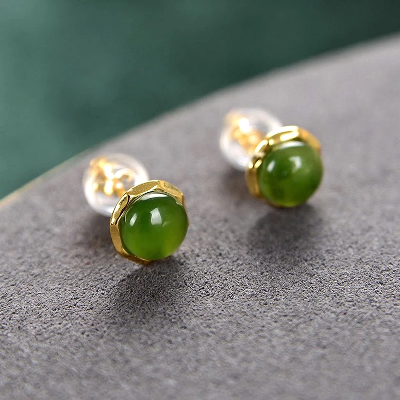 Pair of natural jade stud earrings with clear acrylic earring backs on grey suede surface, demonstrating included ear backs for comfort