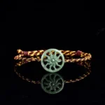 Green jade sun carved pendant on bicolor braided rope bracelet, top-down front view showing mirrored reflection