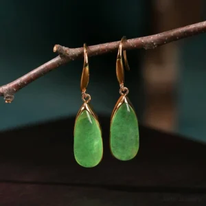 Side profile view of vintage gold tone jade teardrop earrings on dark tabletop, displaying smooth polished jade pendant and elegant gold ear hook detail