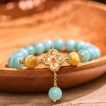 Jade tiger eye prosperity bracelet with four-leaf clover charm displayed on wooden surface, showing turquoise jade beads and golden brown tiger eye stones