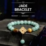 Jade yellow tiger eye prosperity bracelet with metal four-leaf clover charm and dangling jade bead on dark stone background