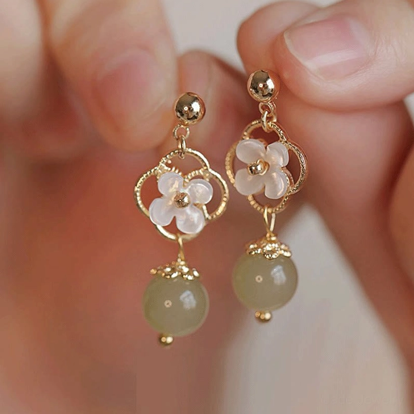 Close-up of jade drop earrings held in hand, showcasing detailed tridacna floral design and dangling jade bead