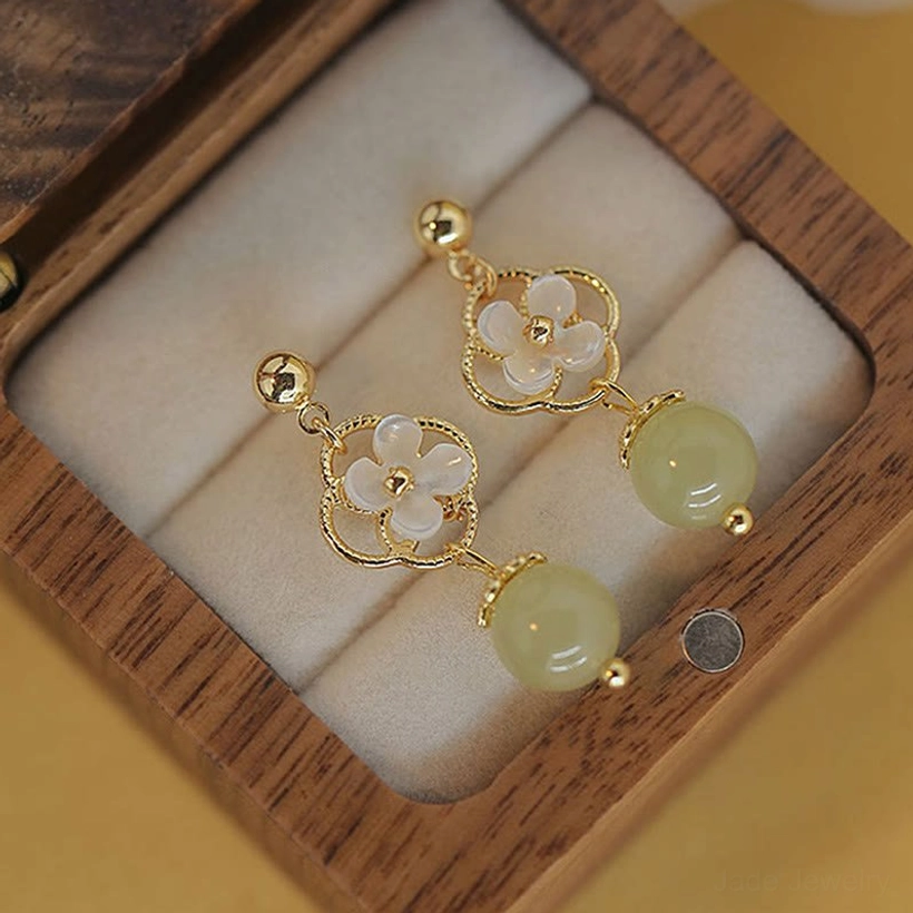 Hetian jade and tridacna flower drop earrings close-up on fingers, detailed view of floral metalwork and gold-tone hardware