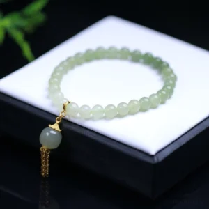 Hetian jade beaded bracelet flat lay on black and white jewelry tray, ombre light green jade beads with sterling silver gold-plated tassel charm