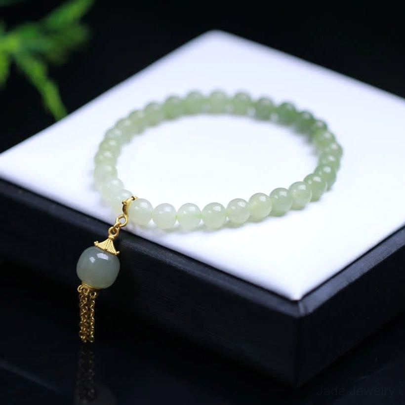 Hetian jade beaded bracelet flat lay on black and white jewelry tray, ombre light green jade beads with sterling silver gold-plated tassel charm