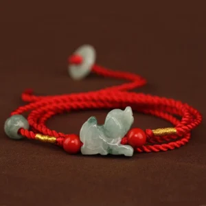 Jade peace buckle belly chain flat lay top view, red braided rope with jade charm, cinnabar beads and gold thread accents on brown background