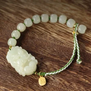 Handcrafted jade zodiac charm bracelet on wooden surface - carved jade pendant and gold fu tag