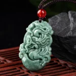 Natural green jade Chinese zodiac dragon pendant with red bead and black cord, overhead view on traditional wooden grille background