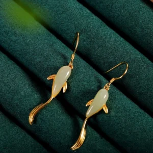 Koi fish jade drop earrings with gold metal frame on dark green velvet, showing smooth polished jade body and curved design