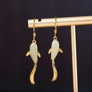 Pair of koi fish jade dangle earrings hanging on metal display rod, featuring bright gold finish and streamlined curved tail